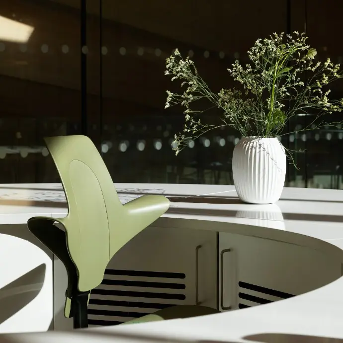 HÅG Capisco Puls in moss groen – perfect voor een frisse, natuurlijke werkplek Groene HÅG Capisco Puls met moss frame aan een wit bureau in een interieur met veel groen en planten