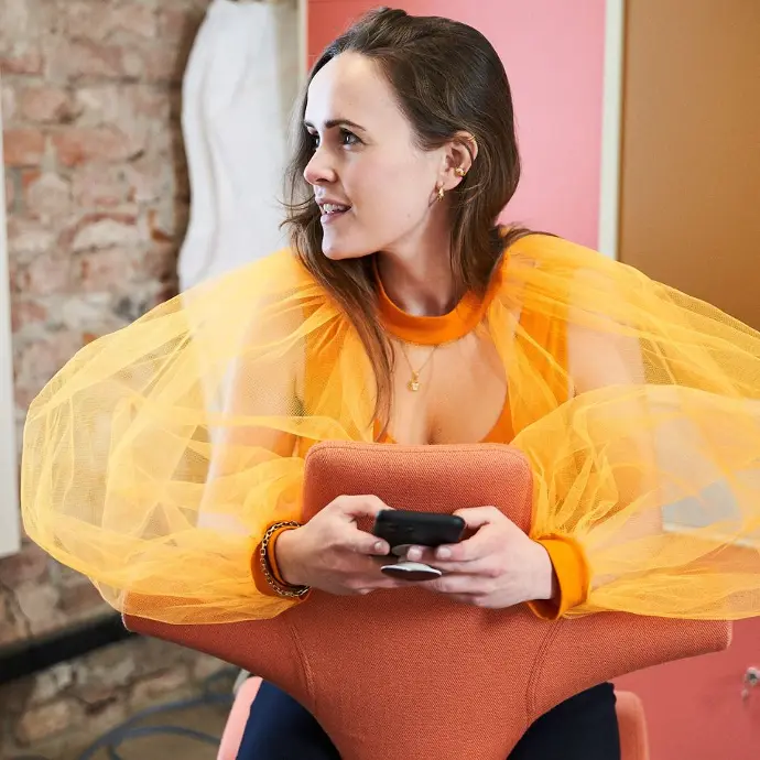 Creatief, kleurrijk en duurzaam werken met de HÅG Capisco 8106 – samenwerking Faebrik Collective Vrouw op kleurrijke oranje HÅG Capisco 8106 stoel, samenwerking met Faebrik Collective